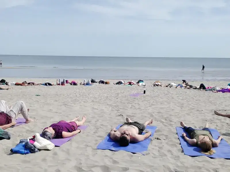 Fila di persone distese su tappetini in spiaggia davanti al mare